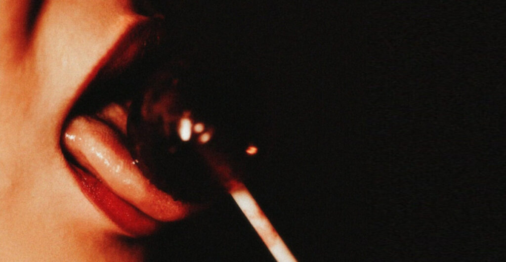 여자가 정액을 빗댄, 검붉은 사탕을 혀로 핥는 모습