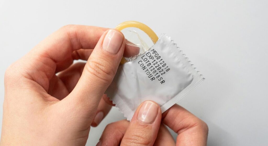 유통기한이 인쇄된 개별 포장지를 손으로 개봉하며 날카로운 물건에 의한 콘돔 실수를 방지하는 모습.