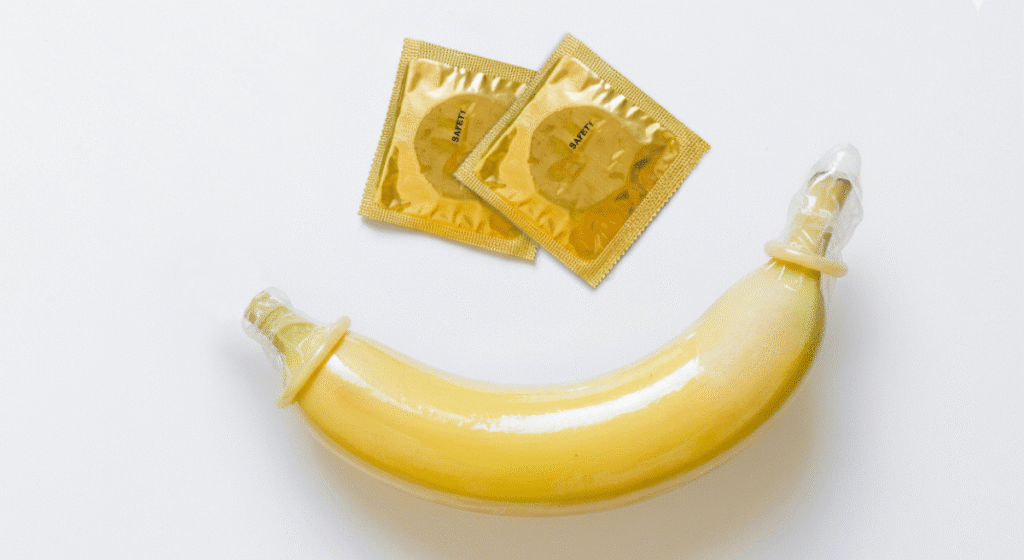 흰 배경에 놓인 바나나 양쪽 끝에 보호구가 씌워져 있고 그 위에 제품 패키지가 놓인 모습. 양방향 더블 딜도 사용 시의 위생과 안전을 강조함.