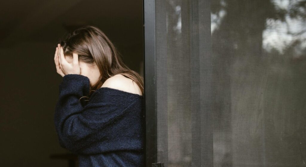 문가에 기대어 얼굴을 감싸 쥐고 성욕 저하와 심리적 부담감에 괴로워하는 여성